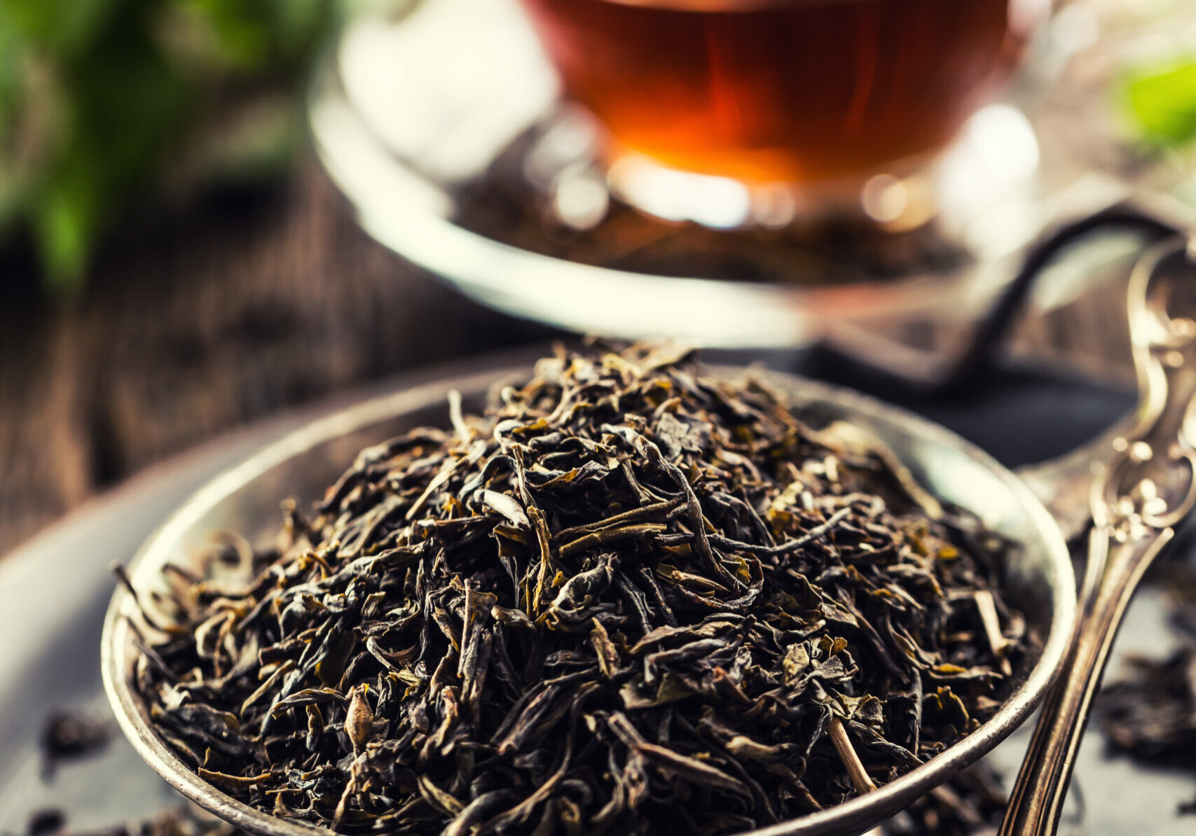 Dried tea leaves in bowl on rustic wooden table.