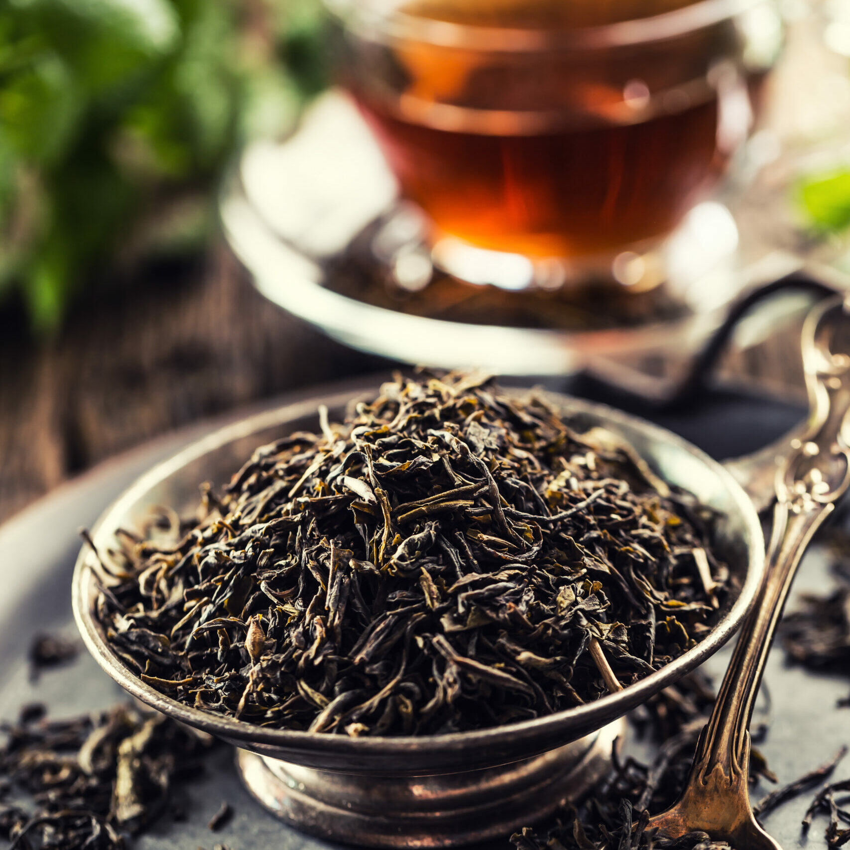 Dried tea leaves in bowl on rustic wooden table.